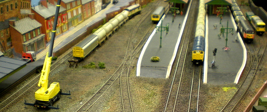 Bridgebury Station's western end, with 37 402 'Bonty Bermo' and a short freight in the yard, a DMU 1212 branchline service, a blue Class 24 (hired in) for the cement service passing a Loadhaul Class 56 on a loaded seacow ballast hoppers, and an InterCity Class 73 tidying up engineering work leftovers - two NGS kit-built PNA ballast wagons in Railtrack green.